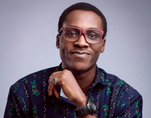 Charming young man in eyeglasses posing confidently with a smile against a purple background.