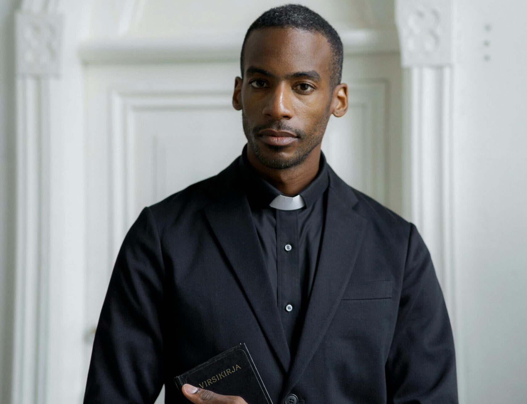 Stylish pastor in a church setting holding a book, contemplating faith and spirituality.